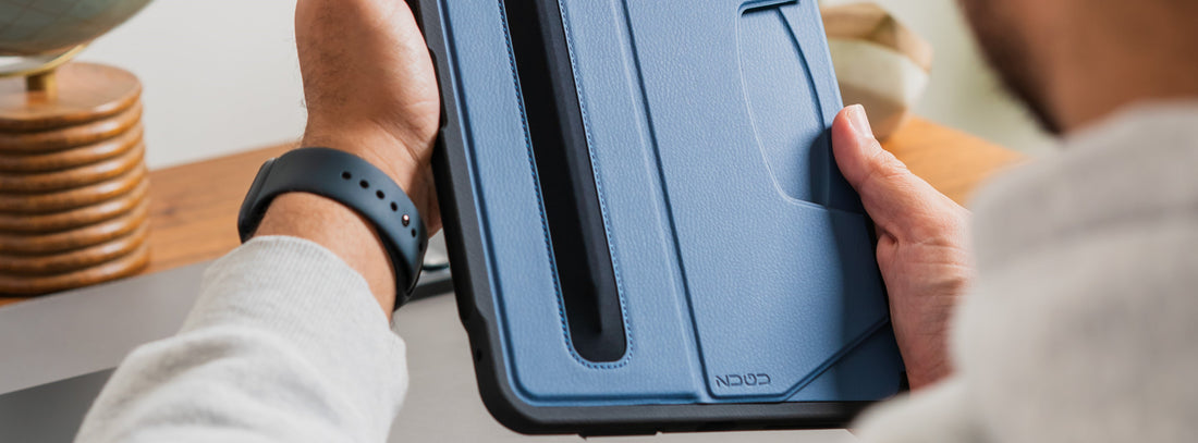 A man holds his iPad in a blue ZUGU case with an attached Apple pencil
