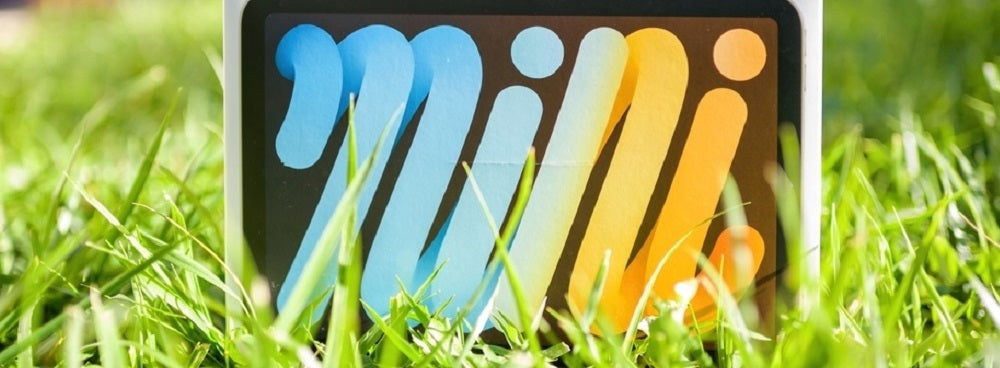 An iPad Mini box with a vibrant logo design displayed outdoors on green grass