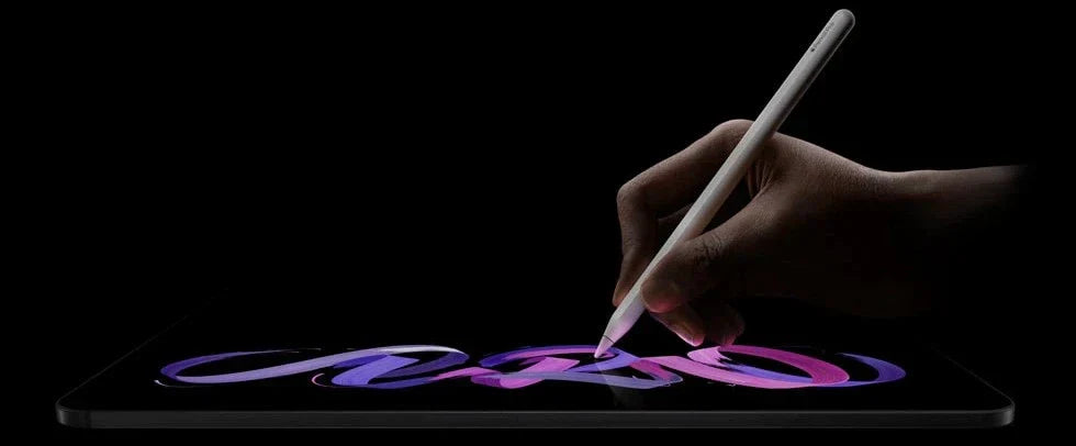 An iPad Pro M5 model laid flat, with a hand holding an Apple Pencil 2, drawing on the screen.
