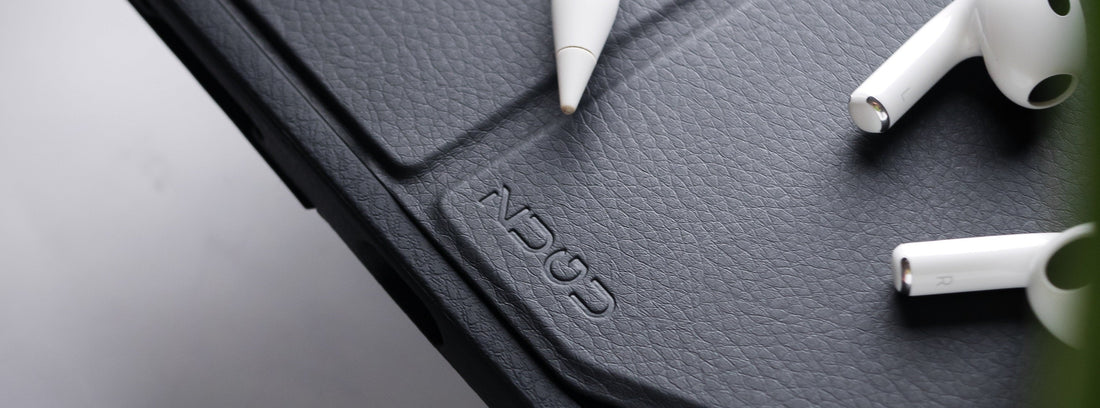 Close-up of a black textured leather iPad case with an engraved "ZUGU" logo, shown with a white Apple Pencil and two white Apple AirPods resting on top