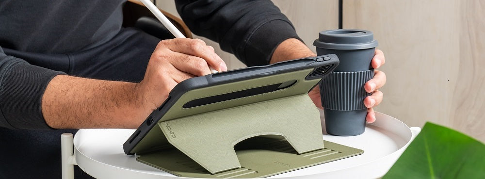 Person using a stylus on a tablet with a stand, next to a reusable coffee cup
