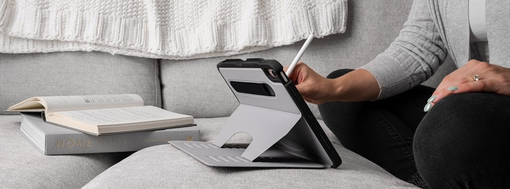Person using an iPad with a protective case and stylus on a grey couch