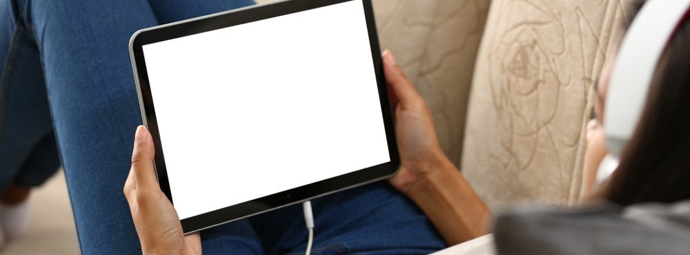 a woman lying on the sofa holding an iPad featuring a blank white screen