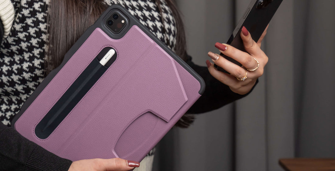 A woman carrying a berry colored ZUGU case with an Apple Pencil, and an iPhone in the other hand, which she is looking at.