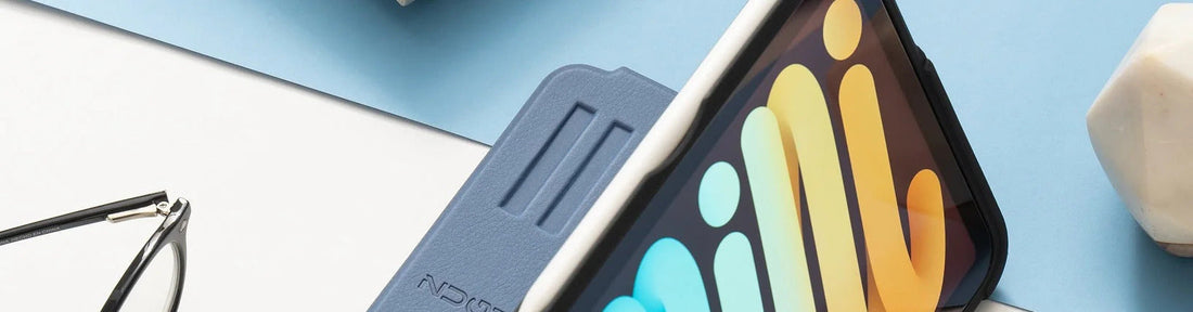 An iPad Mini with a blue Zugu case sits on a white and blue surface next to a pair of glasses and a small white geometric object.