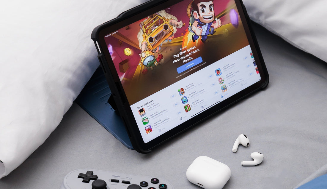  An iPad showing the App Store on its screen, Apple earphones, and a gaming console lying on a bed.