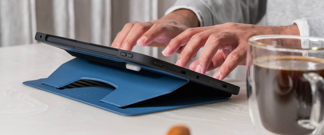 Man typing on an iPad in a ZUGU case, seated at a table with a clear glass mug of coffee