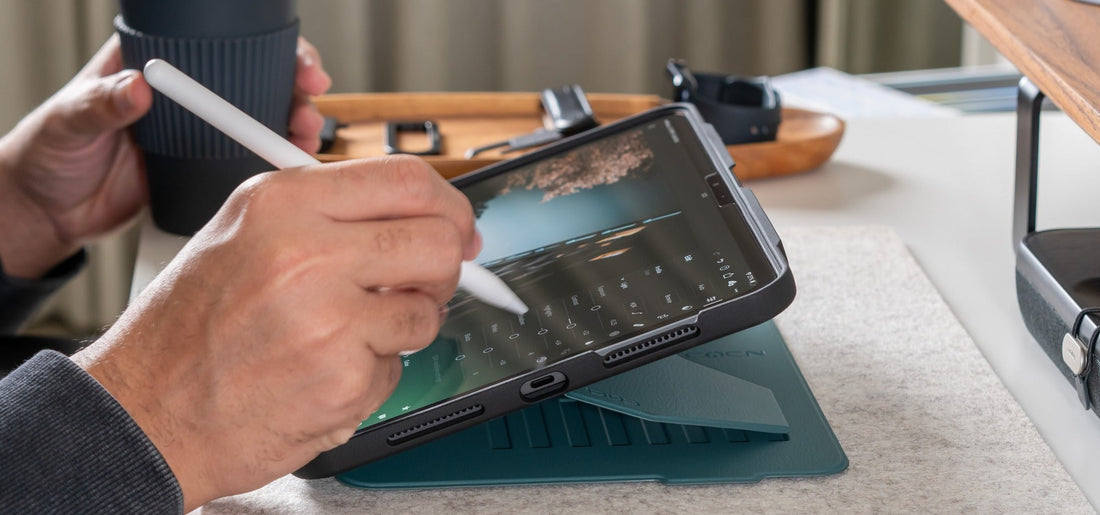 A man holding coffee while using an Apple Pencil on an iPad Pro in a Pine ZUGU case.